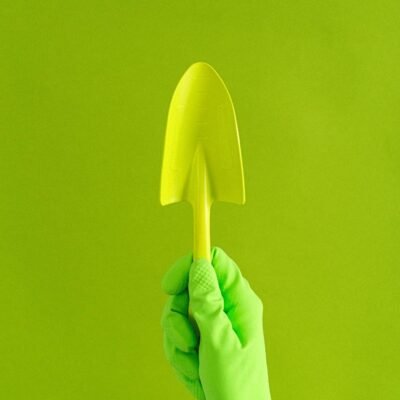 Crop anonymous gardener in rubber glove showing metal trowel against green wall in studio