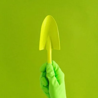 Crop anonymous gardener in rubber glove showing metal trowel against green wall in studio