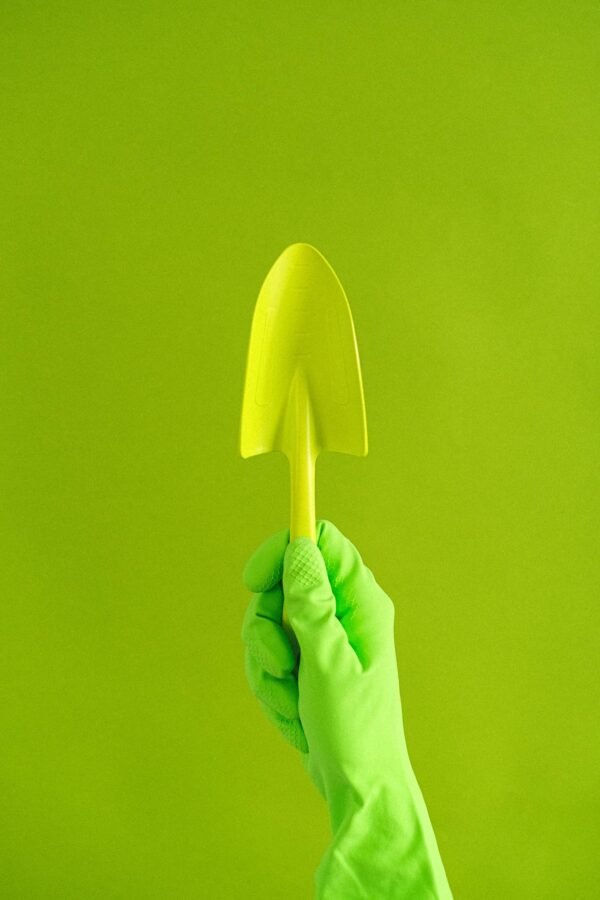 Crop anonymous gardener in rubber glove showing metal trowel against green wall in studio